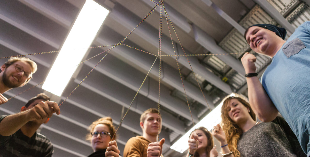 Junge Frauen und Männer halten einzelne Fäden eines Fadennetzes fest.